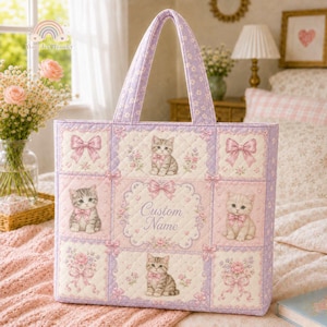 Puede incluir: Un bolso tote acolchado con un patrón floral en tonos lavanda y rosa, decorado con ilustraciones de gatitos y lazos. El panel central incluye un marco decorativo con el texto Custom Name. El bolso cuenta con dos asas a juego y un diseño de cuadrícula.