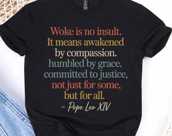 May include: Black t-shirt with the quote "Woke is no insult. It means awakened by compassion. humbled by grace. committed to justice, not just for some, but for all. - Pope Leo XIV" printed in various colors.