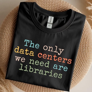 May include: Black t-shirt with the text "The only data centres we need are libraries" in colourful letters. The shirt is made of a soft material and is displayed on a woven surface.