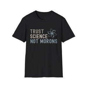 May include: Black t-shirt with the text "TRUST SCIENCE NOT MORONS" in a mix of gray and blue colors. An atom graphic is next to the text. The shirt is a short-sleeved crew neck.