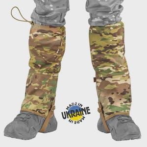 Könnte beinhalten: Tarnmanschetten, getragen über grauen Schuhen und einer Tarnhose. Die Gamaschen haben ein braunes, grünes und beiges Muster. Der Text "MADE IN UKRAINE" ist auf dem Bild aufgedruckt.