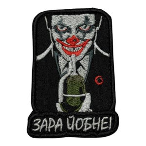 Puede incluir: Parche bordado con un payaso siniestro con labios y ojos rojos, sosteniendo una granada. El diseño está sobre un fondo negro con el texto "ZAPA ЧОБНЕ!" en blanco. También es visible un pequeño círculo rojo.