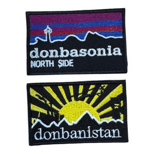 May include: Two rectangular embroidered patches. The top patch features a purple, blue, and red mountain silhouette with the text "donbasonia" and "NORTH SIDE" in white. The bottom patch shows a yellow sunburst over black mountains with "donbanistan" in white.