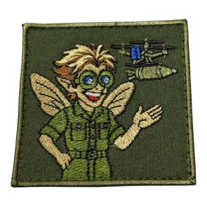 May include: Embroidered patch with a cartoon fairy wearing green goggles and a military uniform. The fairy has wings and is gesturing towards a helicopter and a bomb. The patch is on a green background with a stitched border.