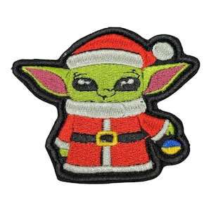 Puede incluir: Parche bordado con un personaje alienígena verde que lleva un gorro de Papá Noel y un traje rojo con cinturón negro y hebilla dorada. El personaje sostiene un pequeño objeto azul y amarillo. El parche tiene un borde negro.