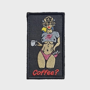 May include: Embroidered patch depicting a cartoon woman holding a coffee cup, wearing a gray top and pink bikini bottoms. The patch has the text "Coffee?" in red. The woman has blonde hair and red lipstick. The patch is rectangular with a black border.