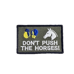 Op de afbeelding: Geborduurde patch met de tekst "DON'T PUSH THE HORSES!" op een olijfgroene achtergrond. De patch toont een witte paardenkop en twee paar bokshandschoenen.