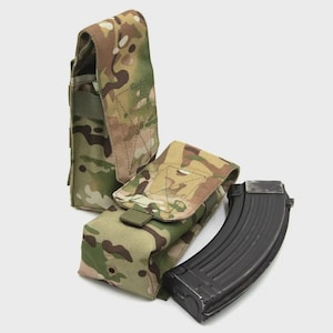 Op de afbeelding: Twee tactische magazijntassen met een camouflagepatroon in beige, bruin en groen. Eén tas staat rechtop, terwijl de andere horizontaal naast een gebogen zwart metalen magazijn voor een geweer ligt.