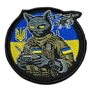 May include: Embroidered patch featuring a cat in military attire, holding a weapon. The design incorporates the Ukrainian flag colors, blue and yellow, and the Ukrainian coat of arms. The patch has a black border.