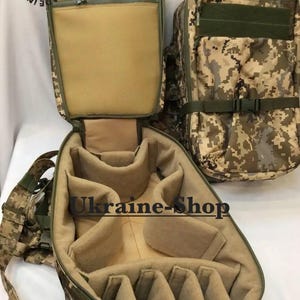 Puede incluir: Una mochila táctica con camuflaje digital y un interior color canela con divisores acolchados ajustables. El exterior tiene un compartimento con cremallera y una correa con hebilla. El texto "MADE IN UKRAINE" y "Ukraine-Shop" es visible.