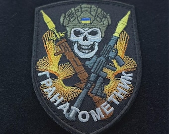May include: Embroidered patch featuring a skull wearing a helmet with a Ukrainian flag. The patch includes a rifle, a rocket launcher, and text in Cyrillic script. The patch is black with gold, brown, blue, and white details.