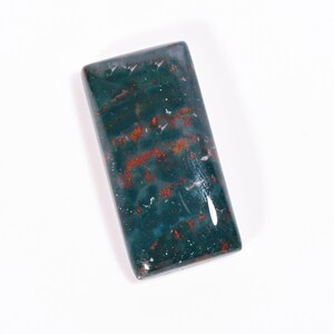 Könnte beinhalten: Ein rechteckiger Blutstein-Cabochon mit einer polierten, glatten Oberfläche. Der Stein weist eine tiefdunkelgrüne Grundfarbe mit verstreuten, unregelmäßigen Einschlüssen von leuchtend roten und orangen Flecken im gesamten mineralischen Körper auf.