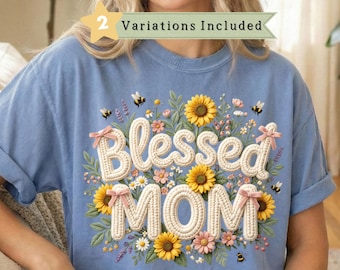 May include: A light blue t-shirt with the words "Blessed MOM" in a floral design. The design includes sunflowers, small flowers, bees, and pink bows. The shirt has rolled-up sleeves.