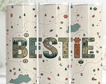 May include: A beige tumbler with a map design and the word "BESTIE" in a decorative font. The letters are filled with camping and hiking-themed illustrations, including tents, paw prints, and trees. The tumbler is designed for cold beverages.
