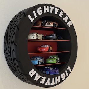 May include: A black, tyre-shaped shelf unit with the word "LIGHTYEAR" in white. It displays toy race cars in various colours, including red, blue, and green. The interior shelves are red.