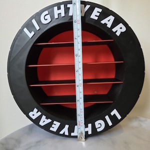 May include: A black and red circular shelf with the text "LIGHTYEAR" in white. The shelf has four red shelves inside and measures approximately 25 cm in height.