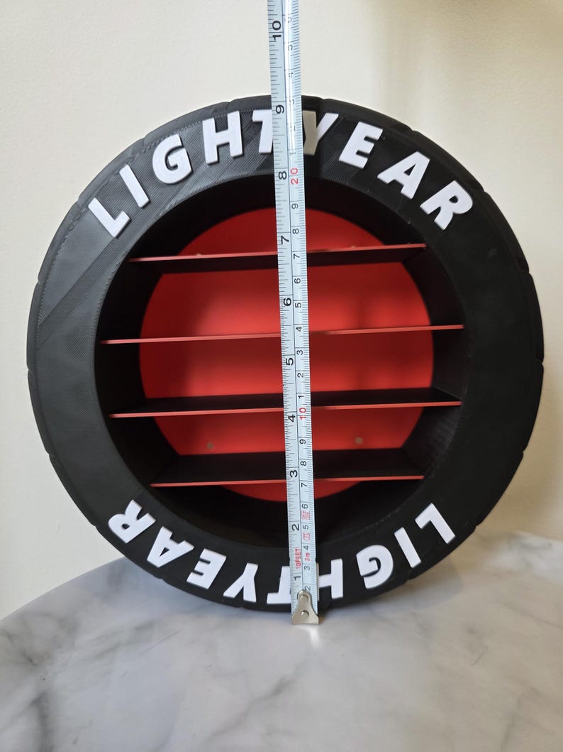 May include: A black and red circular shelf with the text "LIGHTYEAR" in white. The shelf has four red shelves inside and measures approximately 25 cm in height.