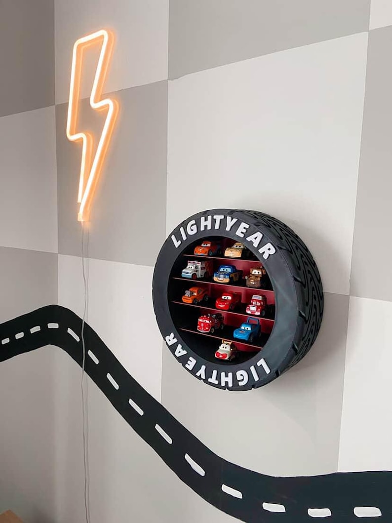 May include: A black tyre-shaped shelf displaying toy cars, with the word "LIGHTYEAR" in white. A neon orange lightning bolt is mounted on the wall. A black road design with white dashed lines is painted on the wall.