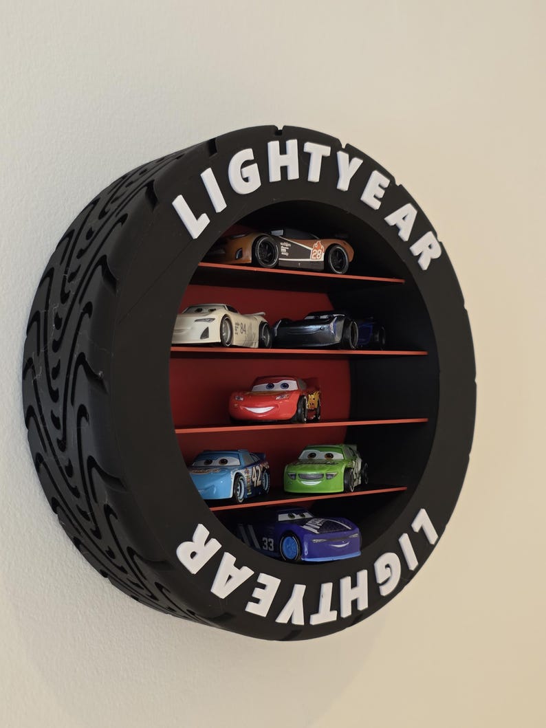 May include: A black, tyre-shaped shelf unit with the word "LIGHTYEAR" in white. It displays toy race cars in various colours, including red, blue, and green. The interior shelves are red.