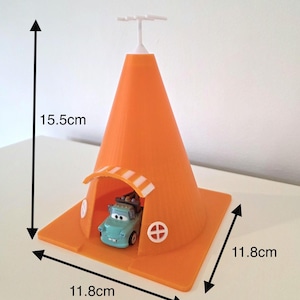 May include: An orange plastic toy traffic cone, 15.5cm tall and 11.8cm wide, with a small blue toy car inside. The cone has a white top and a small arched entrance. The base has two white circular designs.