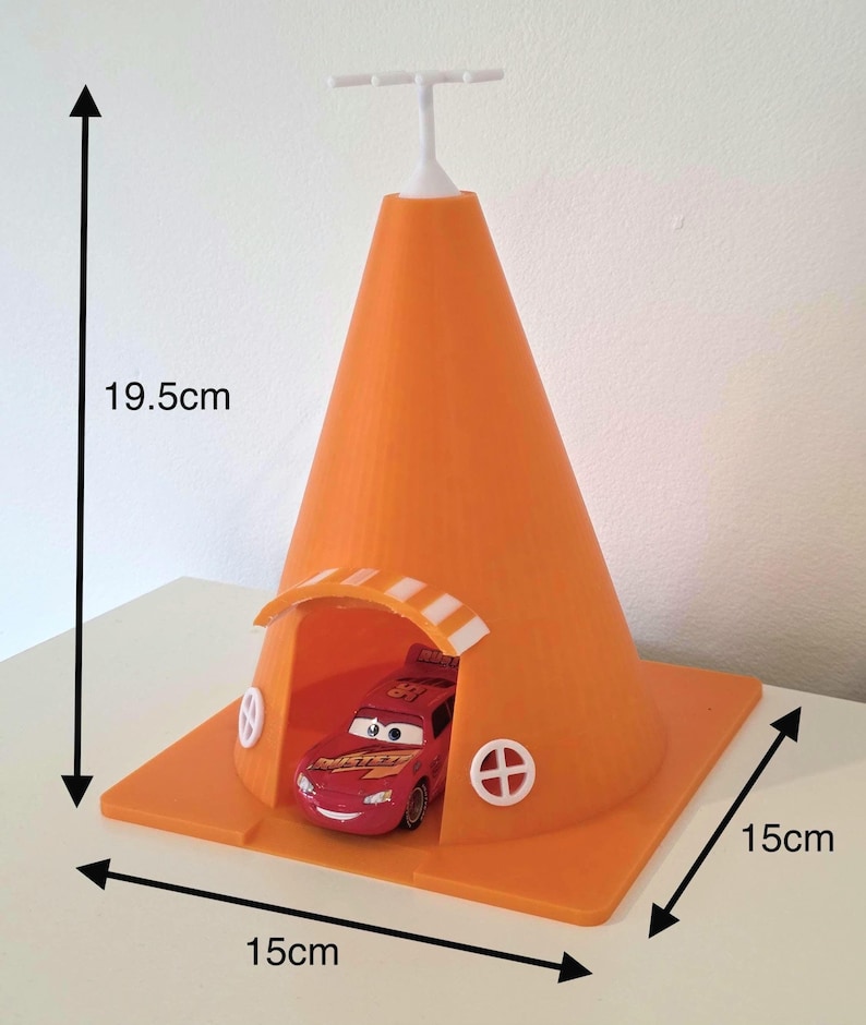 May include: An orange, cone-shaped toy structure with a red race car inside. The structure is 19.5 cm tall and 15 cm wide, with a white top and a small arched opening. The car is red with the number 95.