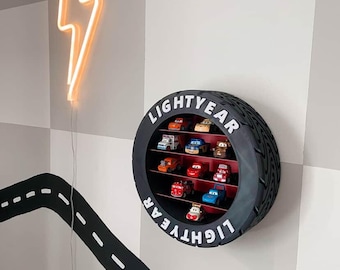 Könnte beinhalten: Ein kreisförmiges Wandregal in Form eines schwarzen Reifens mit rotem Innenraum, das oben und unten den weißen Schriftzug "LIGHTYEAR" trägt. Das Regal enthält zehn kleine Spielzeugautos, die auf drei horizontalen Ebenen angeordnet sind.