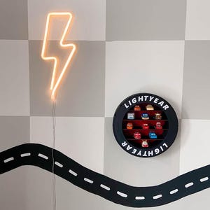 May include: A neon orange lightning bolt wall decoration and a black circular display case with the word "LIGHTYEAR" and toy cars. A black road design is painted on the wall.