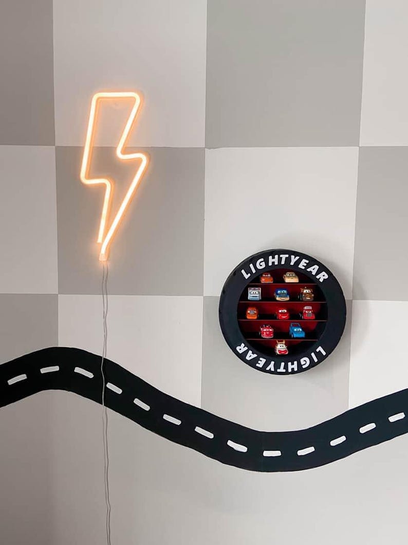 May include: A neon orange lightning bolt wall decoration and a black circular display case with the word "LIGHTYEAR" and toy cars. A black road design is painted on the wall.