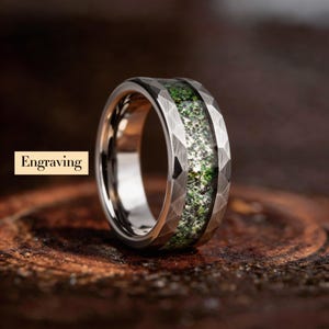 May include: A silver ring with a faceted, textured band and a central inlay of green and white speckled material. The word "Engraving" is in a tan rectangle in the image.
