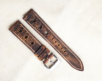 Puede incluir: Dos correas de reloj de cuero marrón desgastado con costuras blancas y múltiples perforaciones circulares. Una correa tiene una hebilla plateada. Las correas son para un reloj y se muestran sobre un fondo neutro.