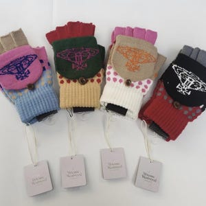 Op de afbeelding: Vier paar vingerloze gebreide handschoenen met omslagwanten, elk voorzien van een Vivienne Westwood orb-logo op de flap en een klein knoopje. De handschoenen zijn verkrijgbaar in blauw, beige, crème en rood en zijn voorzien van merkkaartjes.