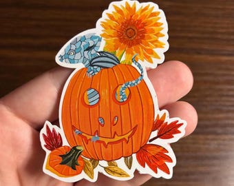 Peut inclure: Un autocollant sur le thème d'Halloween représentant une citrouille orange avec un visage souriant, un serpent bleu et gris, et une grande fleur orange. L'autocollant comprend également des feuilles d'automne et une petite citrouille.
