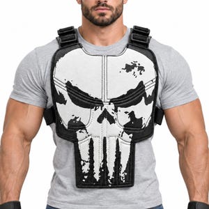 May include: A black and white chest rig featuring a stylised skull graphic on the front panel. The gear includes adjustable black nylon straps with plastic buckles, a padded construction, and vertical stitching details across the white skull design.
