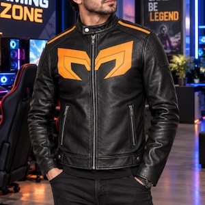 May include: A black leather jacket featuring a mandarin collar with a snap button, a full-length front zip, and two zipped side pockets. The chest displays a large, stylised orange graphic design, with matching orange stripes along the shoulders.