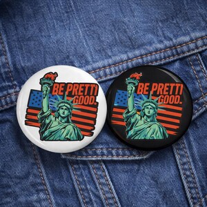 May include: Two circular badges with a patriotic design. One is white, the other black. Both display the Statue of Liberty, an American flag, and the words "BE PRETTI GOOD."
