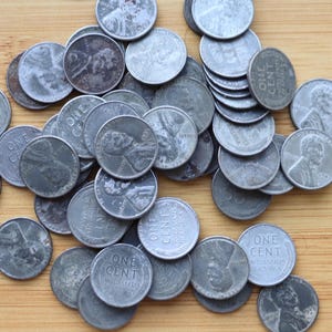 May include: A collection of circulated United States one-cent coins, also known as pennies, scattered on a wooden surface. The coins display the profile of Abraham Lincoln and the words "ONE CENT" and "UNITED STATES OF AMERICA".