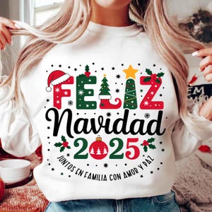 Puede incluir: Sudadera blanca con un diseño navideño. El diseño incluye las palabras "Feliz Navidad" en rojo y verde, el año "2025" y gráficos festivos como un gorro de Papá Noel, un árbol de Navidad y adornos.