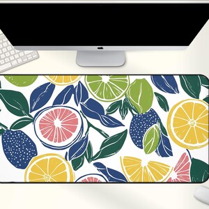 May include: Rectangular desk mat featuring a vibrant pattern of citrus fruits and leaves in shades of yellow, green, pink, and blue on a white background. The mat is designed to fit under a computer and keyboard.