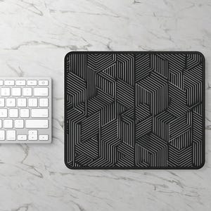 May include: Black and white geometric pattern mousepad with a matching white keyboard on a marble surface. The mousepad features a repeating design of angled lines creating a 3D effect. The keyboard is a standard layout.