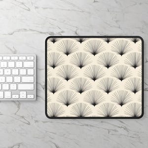May include: A rectangular mousepad with a black border and a cream-colored surface. The surface features a repeating pattern of black fan-like shapes. A white keyboard is visible on the left side of the image.