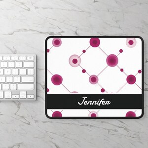 May include: A rectangular mousepad with a white background featuring a pattern of pink circles and lines. A black banner at the bottom displays the name "Jennifer" in white script. A white keyboard is visible on the left.
