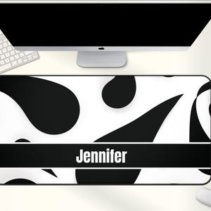 May include: A rectangular desk mat with a black and white abstract design. The mat features a black band with the name "Jennifer" in white. A computer monitor, keyboard, and mouse are visible in the background.