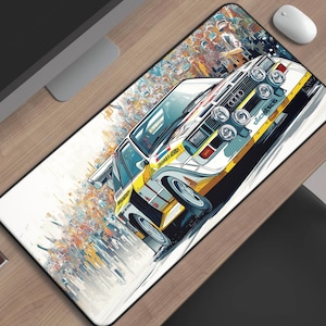 May include: A rectangular mouse pad featuring a stylized illustration of a white and yellow Audi Quattro rally car. The car has multiple headlights and sponsor decals. The background has colorful abstract elements. A white mouse and a cup of coffee are visible.