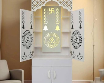 Op de afbeelding: Witte houten kast met ingewikkelde uitgesneden ontwerpen, met een gewelfde bovenkant en twee deuren. De kast heeft een centraal paneel met verlichte symbolen en planken. De deuren zijn versierd met cirkelvormige patronen en belmotieven. De kast staat op vier schuine poten.