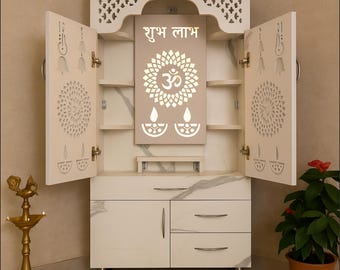 May include: A white wooden cabinet with open doors, featuring intricate cut-out designs and a central panel with the text "शुभ लाभ" and an Om symbol. The cabinet has shelves and drawers, with a marble-like pattern on the front.