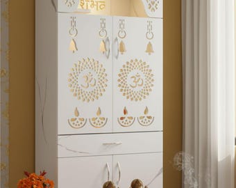 Op de afbeelding: Een witte kast met ingewikkelde uitgesneden ontwerpen, met het woord "शुभ" in goud. De kast heeft twee deuren met Om-symbolen en belletjes. Twee gouden beelden staan op een houten platform voor de kast.