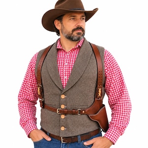 Op de afbeelding: Een bruine vilten cowboyhoed, een rood-wit geruit overhemd met lange mouwen en een grijs wollen vest met vier lichte knopen. Over het vest wordt een bruine lederen schouderholster met verstelbare riemen en metalen gespen gedragen.