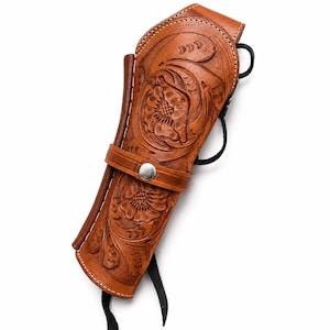 Peut inclure: Un étui en cuir beige orné de motifs floraux gravés et gaufrés. L'étui comprend une sangle horizontale fixée par un bouton-pression en métal argenté et des lacets en cuir noir qui dépassent du bas et des côtés de l'objet.