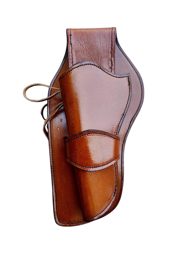 May include: A brown leather holster with a glossy finish. The holster features a curved design with stitched edges and a flap to secure a firearm. A leather strap is visible on the side.