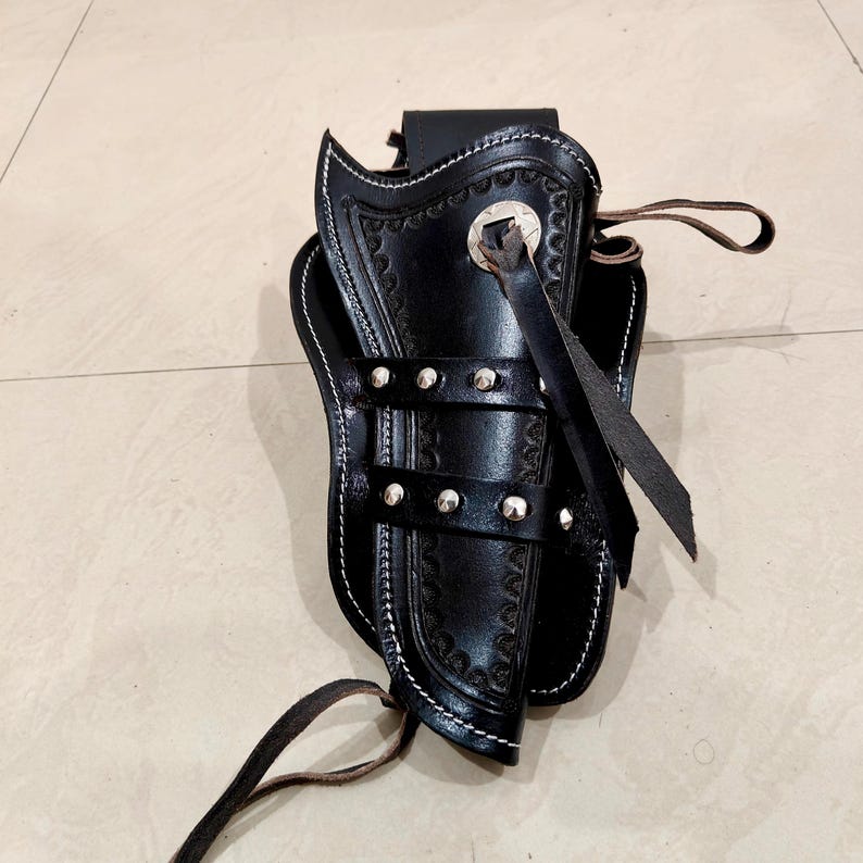 Peut inclure: Un &eacute;tui en cuir noir avec des coutures d&eacute;coratives et des clous argent&eacute;s. L'&eacute;tui pr&eacute;sente un motif en relief d&eacute;taill&eacute; et une lani&egrave;re en cuir. Les bords sont finis avec des coutures blanches.